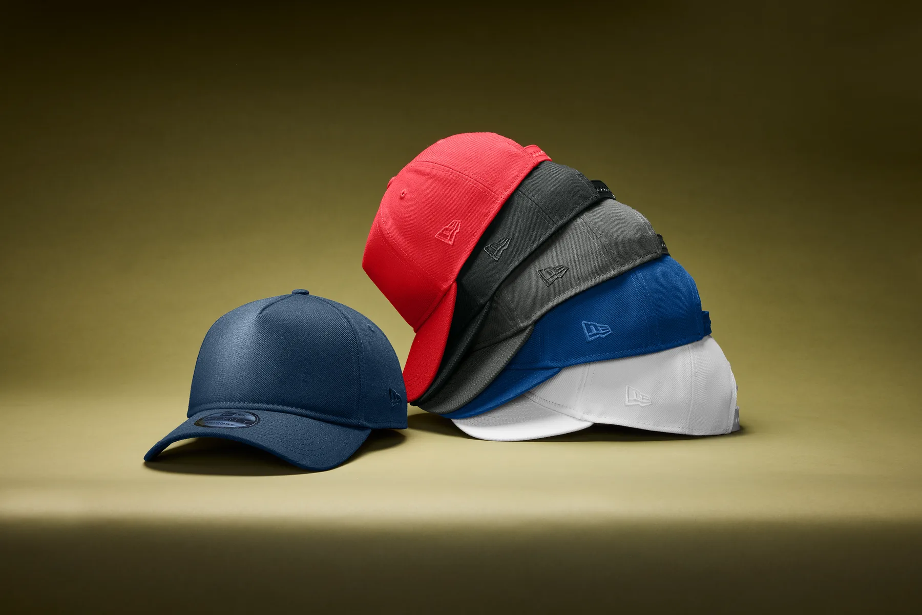 A stack of six structured caps in navy, red, black, graphite, royal blue, and white — the same style in every colorway, the kind of product line a bulk order stocks in depth or a print-on-demand store offers one order at a time.